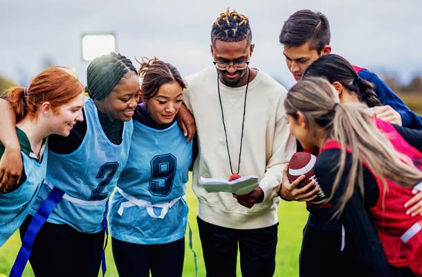 students huddle in closely as they take instructions from their coach during a game of flag football